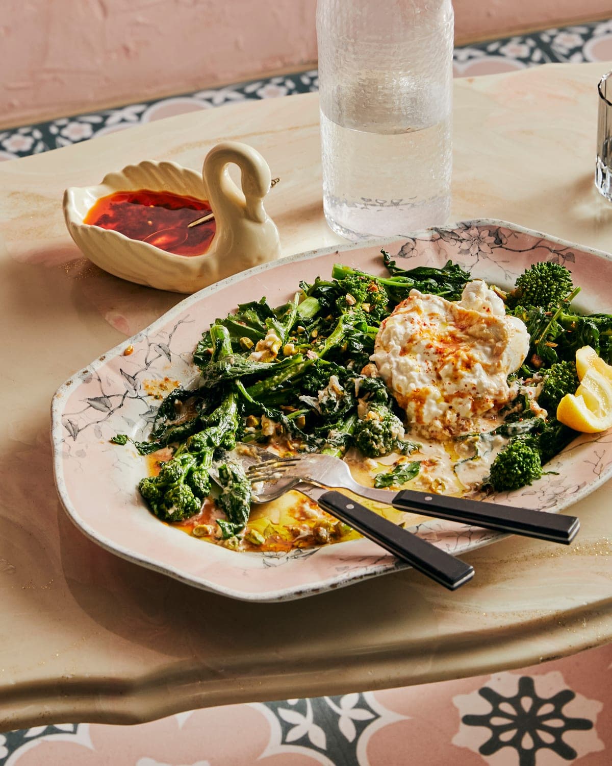 Sautéed rapini with torn burrata, lemon, and pistachios on a pink platter